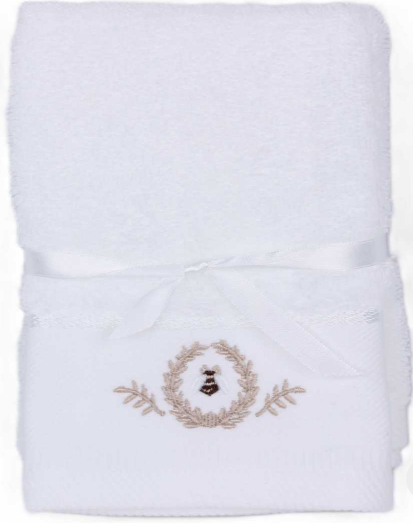 A folded white cotton bath towel with a matching white satin ribbon tied in a bow. The bottom edge features a small beige embroidered design of a bee framed by a laurel wreath.