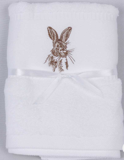 A folded white towel with a brown embroidered bunny face on the upper section and a white satin ribbon tied around the middle, shown on a light gray background.