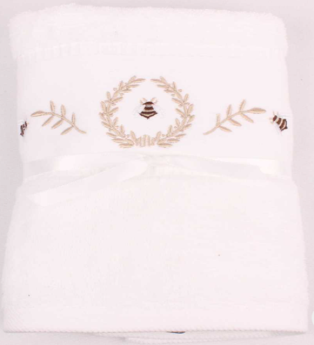 A folded white cotton bath towel featuring embroidered designs of two bees and a gold leaf wreath in the center, with a white satin ribbon tied in a bow at the bottom.