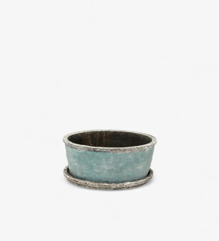 A small round planter pot with a textured, distressed teal-green exterior and a rustic silver-toned rim, sitting on a matching saucer against a plain white background.